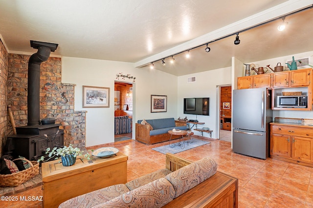 living area featuring light tile patterned floors, visible vents, vaulted ceiling, and a wood stove