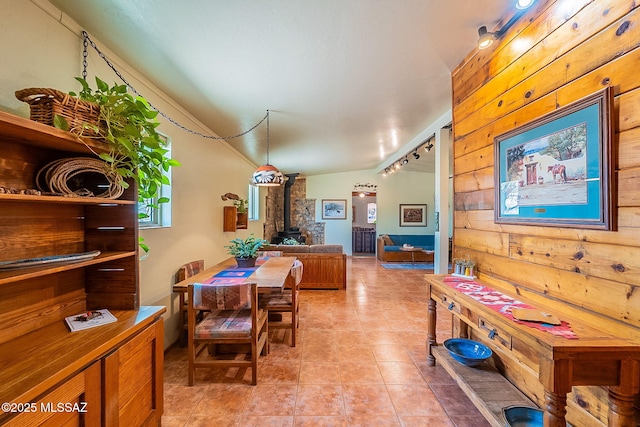 dining area with wood walls, track lighting, a wood stove, vaulted ceiling, and light tile patterned floors