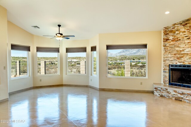 unfurnished living room with baseboards, visible vents, finished concrete floors, a ceiling fan, and a stone fireplace