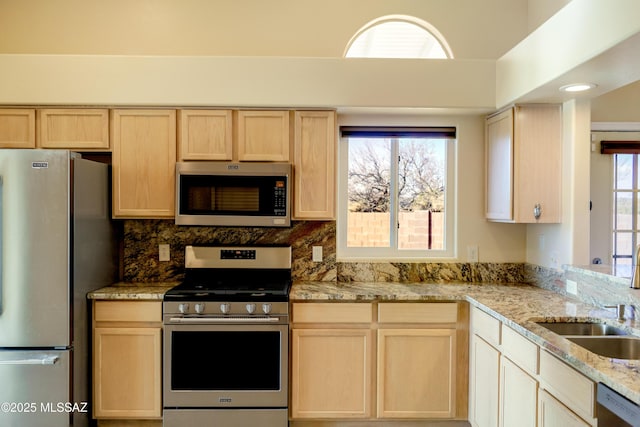 kitchen with light stone counters, light brown cabinetry, stainless steel appliances, and a sink