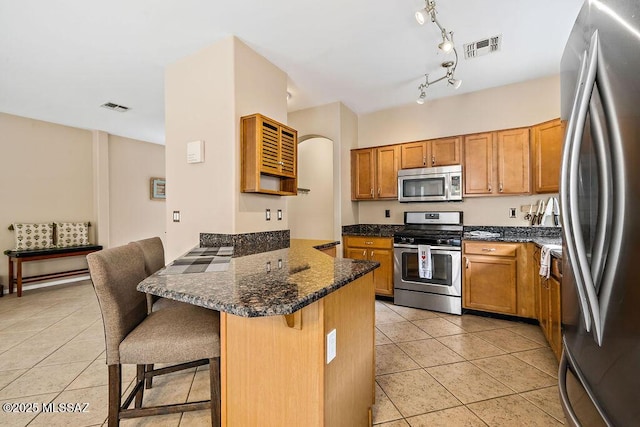 15046 S Harry Truman Pl, Sahuarita, AZ 85629 - kitchen with appliances with stainless steel finishes, a peninsula, light tile patterned flooring, a breakfast bar area, and brown cabinets
