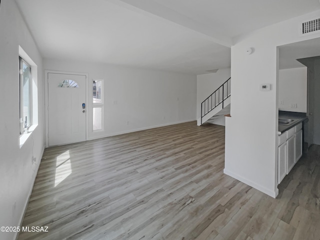 6588 Calle La Paz Unit C, Tucson, AZ 85715 - unfurnished living room featuring light wood finished floors, baseboards, visible vents, and stairway