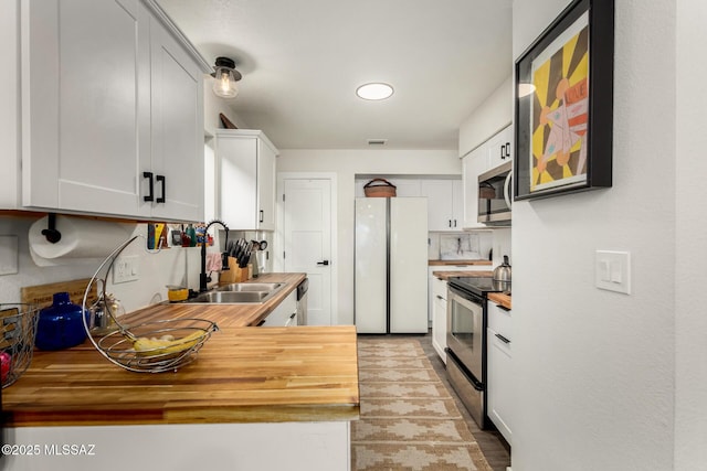 kitchen featuring butcher block countertops, white cabinets, visible vents, stainless steel appliances, and a sink