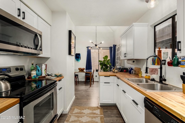 kitchen featuring a sink, wood counters, a notable chandelier, appliances with stainless steel finishes, and wood finished floors