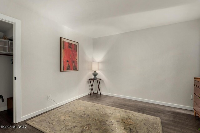 unfurnished bedroom with a spacious closet, baseboards, and wood finished floors