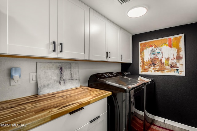 laundry area featuring independent washer and dryer, cabinet space, a textured wall, and baseboards