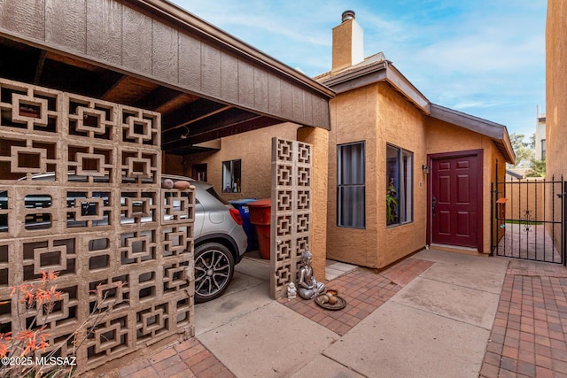 view of side of property featuring stucco siding, a chimney, fence, and a gate