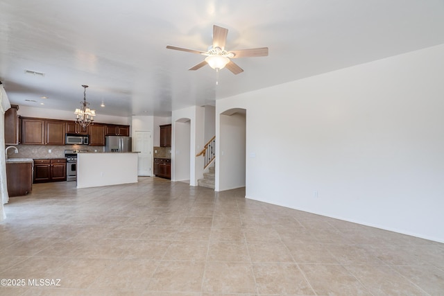 unfurnished living room with a sink, arched walkways, ceiling fan with notable chandelier, and visible vents