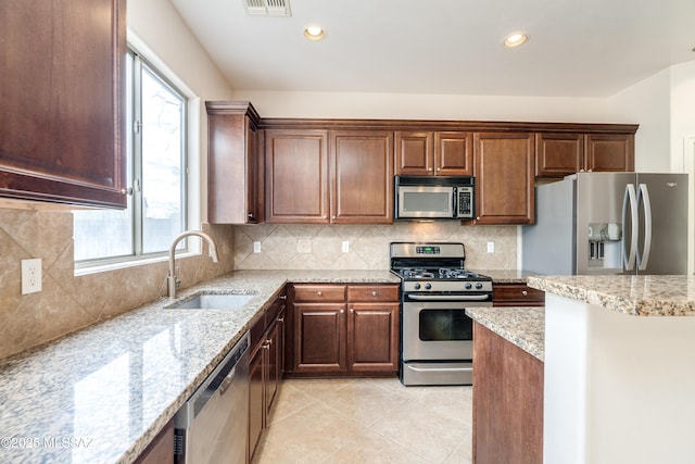 kitchen featuring light stone counters, a sink, appliances with stainless steel finishes, light tile patterned floors, and decorative backsplash