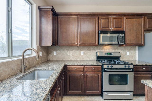 kitchen featuring stainless steel appliances, backsplash, a sink, light stone countertops, and dark brown cabinets