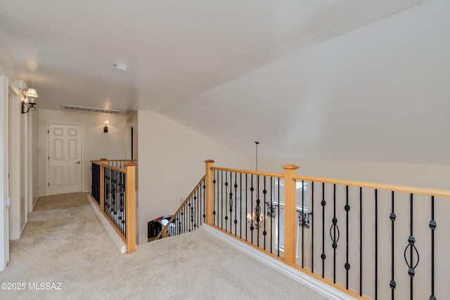 corridor with carpet floors, an upstairs landing, visible vents, and vaulted ceiling