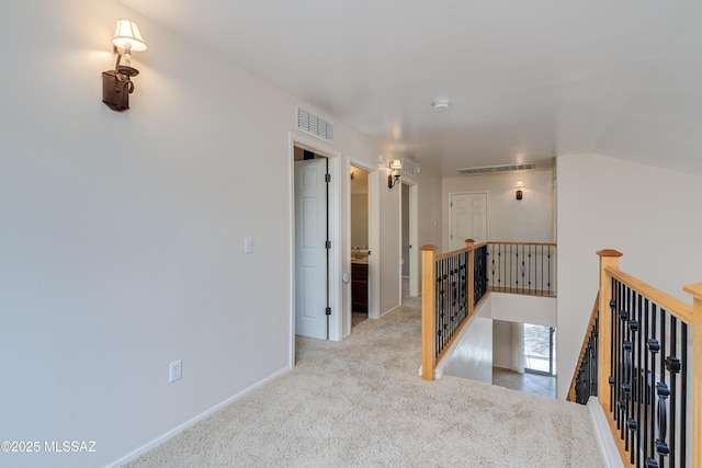 hallway with visible vents, an upstairs landing, carpet floors, and vaulted ceiling