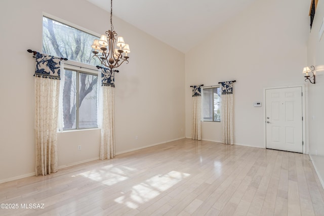 interior space with an inviting chandelier, high vaulted ceiling, baseboards, and wood finished floors