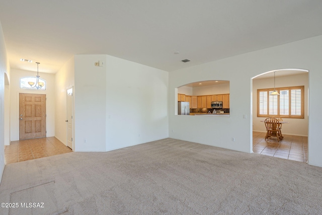 unfurnished living room with light colored carpet, arched walkways, light tile patterned floors, and visible vents