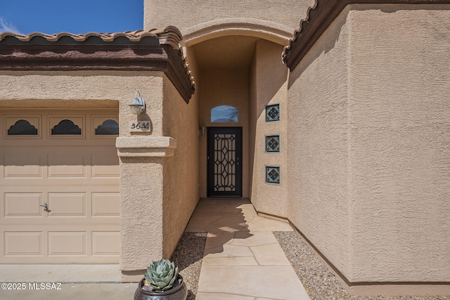 entrance to property with a garage and stucco siding