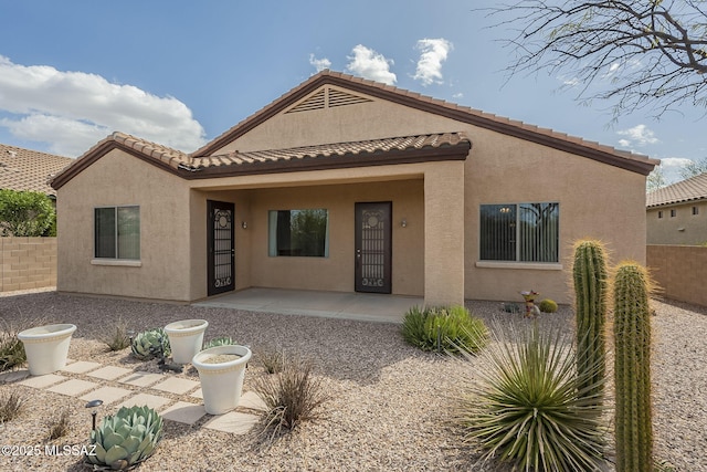 rear view of property featuring stucco siding, a tiled roof, and fence