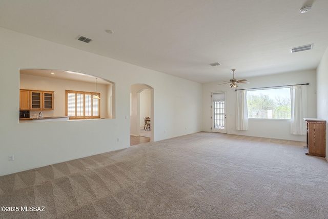 spare room with a healthy amount of sunlight, ceiling fan, light colored carpet, and visible vents