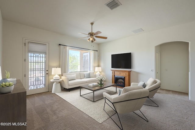living room with visible vents, a glass covered fireplace, ceiling fan, arched walkways, and carpet flooring