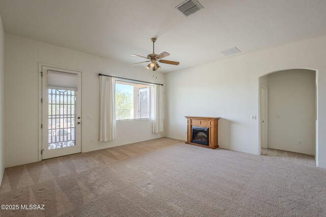 unfurnished living room featuring carpet flooring, ceiling fan, arched walkways, a glass covered fireplace, and visible vents