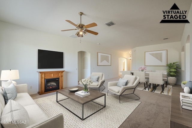 living area with visible vents, a glass covered fireplace, wood finished floors, ceiling fan, and arched walkways