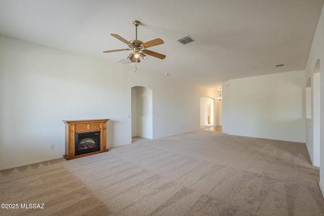 unfurnished living room featuring light colored carpet, arched walkways, a glass covered fireplace, a ceiling fan, and visible vents