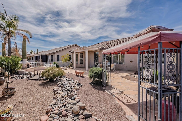 back of property featuring fence, a tiled roof, a gazebo, stucco siding, and a patio area