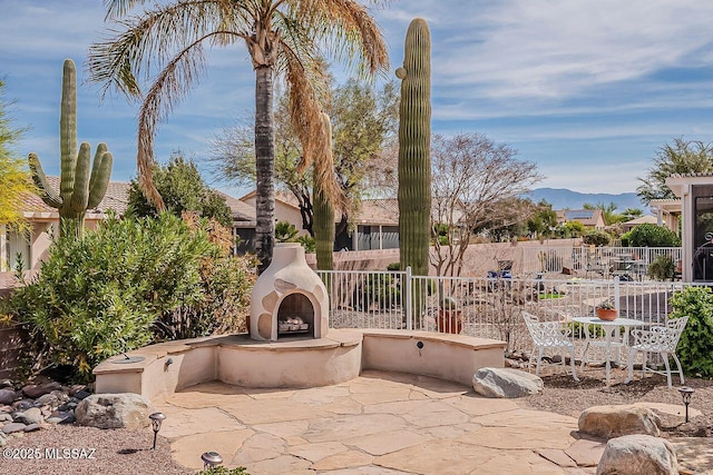 view of patio with an outdoor fireplace, a mountain view, and fence