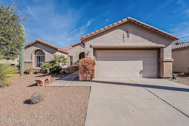 mediterranean / spanish home with driveway, a tile roof, a garage, and stucco siding