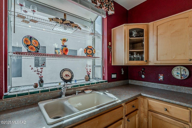kitchen featuring glass insert cabinets, dark countertops, a sink, and light brown cabinets