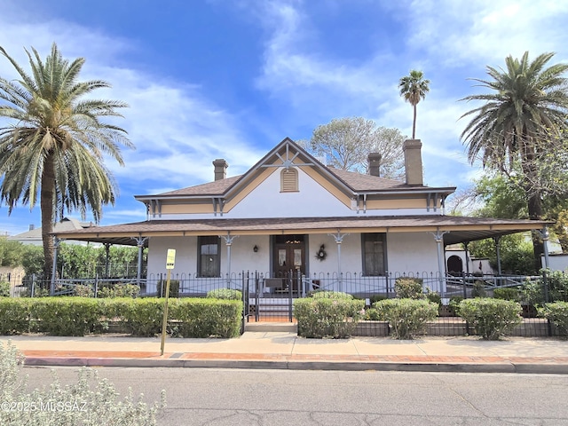 country-style home with a fenced front yard, a chimney, stucco siding, and covered porch