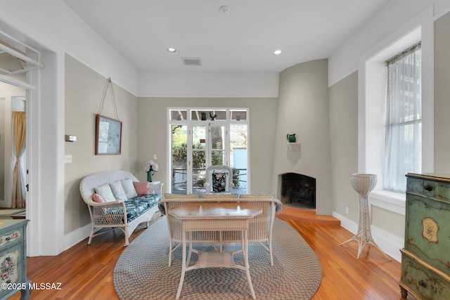 living room with a fireplace with raised hearth, visible vents, baseboards, and light wood-style flooring