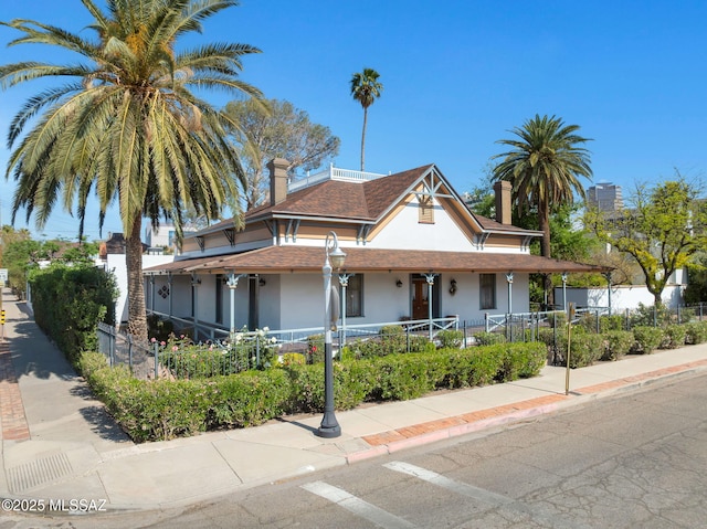 farmhouse-style home with a fenced front yard, a chimney, covered porch, and stucco siding