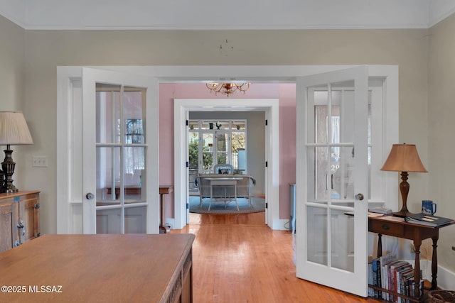 doorway featuring an inviting chandelier, light wood-style flooring, ornamental molding, french doors, and baseboards