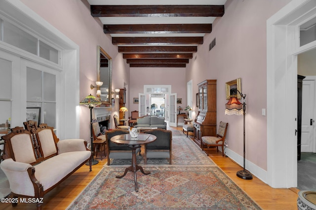 living area with french doors, visible vents, light wood finished floors, and beam ceiling