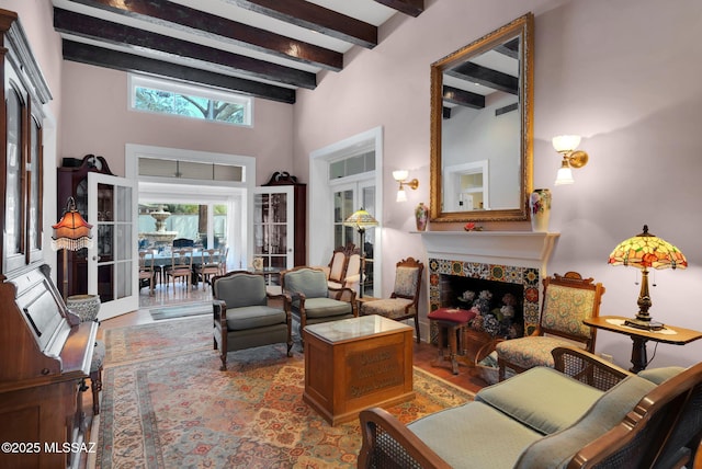 living room featuring a fireplace, a towering ceiling, beamed ceiling, and wood finished floors
