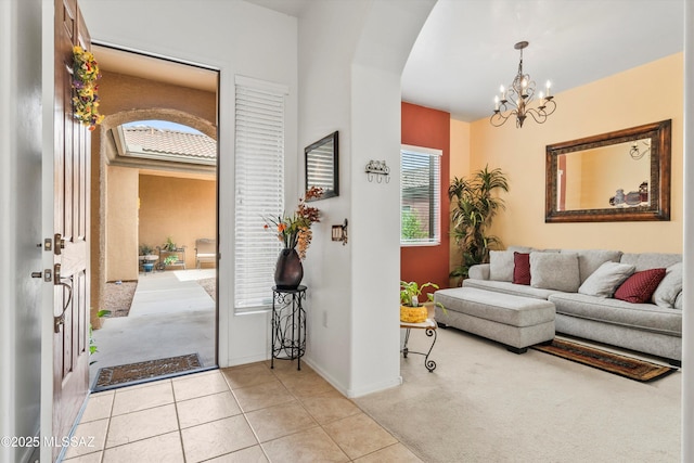 entrance foyer with a notable chandelier, baseboards, light tile patterned floors, light colored carpet, and arched walkways