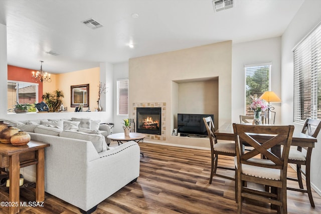 living area with an inviting chandelier, dark wood-type flooring, a tiled fireplace, and visible vents