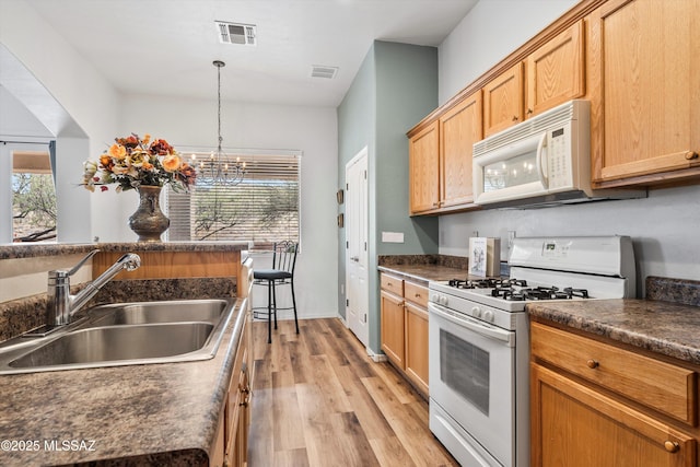 kitchen featuring white appliances, dark countertops, visible vents, and a sink