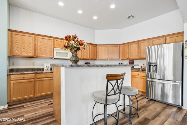 kitchen featuring stainless steel fridge with ice dispenser, white microwave, visible vents, and wood finished floors