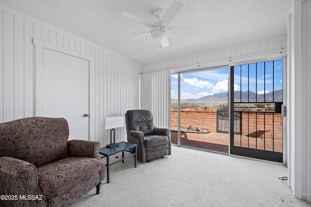 sitting room featuring a textured ceiling, carpet floors, a mountain view, and a ceiling fan