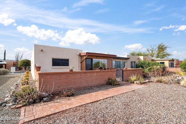 pueblo revival-style home featuring a fenced front yard, a gate, and stucco siding