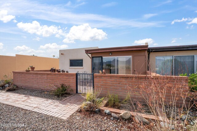 back of property with stucco siding, a gate, and a fenced front yard