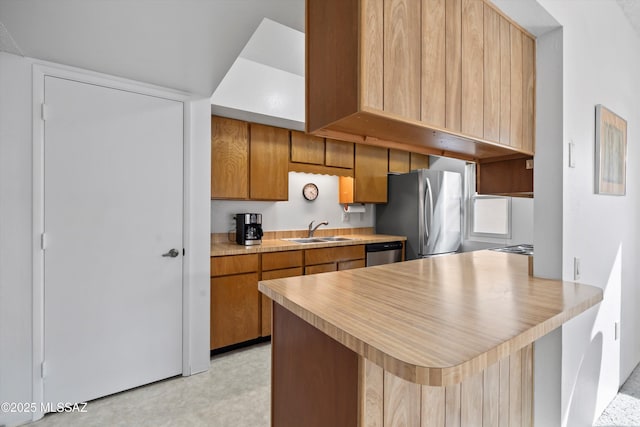 kitchen with light countertops, a peninsula, appliances with stainless steel finishes, a sink, and brown cabinetry