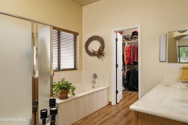 full bath featuring a spacious closet, vanity, a garden tub, and wood finished floors