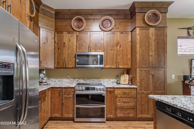 kitchen featuring light stone countertops, brown cabinets, light wood-type flooring, and appliances with stainless steel finishes
