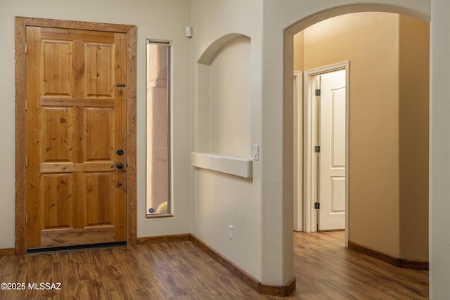 entryway featuring baseboards, arched walkways, and wood finished floors