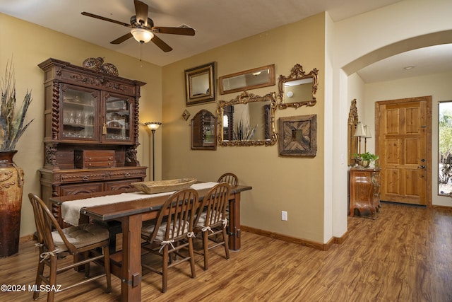 dining area featuring light wood-type flooring, arched walkways, baseboards, and ceiling fan
