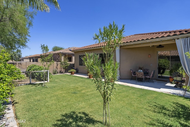 rear view of house with a tiled roof, stucco siding, fence, and a yard