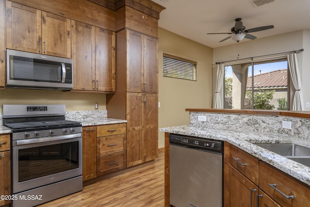 kitchen with a ceiling fan, appliances with stainless steel finishes, brown cabinets, and light wood-type flooring
