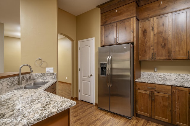 kitchen featuring a sink, light stone countertops, light wood-style flooring, stainless steel refrigerator with ice dispenser, and arched walkways